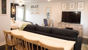 Una sala moderna con un sofá, una mesa de comedor de madera con sillas, un televisor y un espejo.