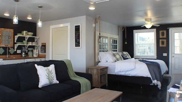 Un espacio habitable compacto con sofá, cama, una mesita y ventilador de techo.