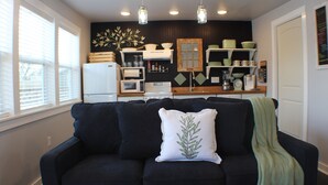 Una sala de estar con un sofá de color oscuro, un cojín blanco con diseño de hojas y una manta verde.
