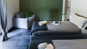 Habitación de hotel moderna con una cama grande, un sofá más pequeño, una lámpara de pie y un radiador.