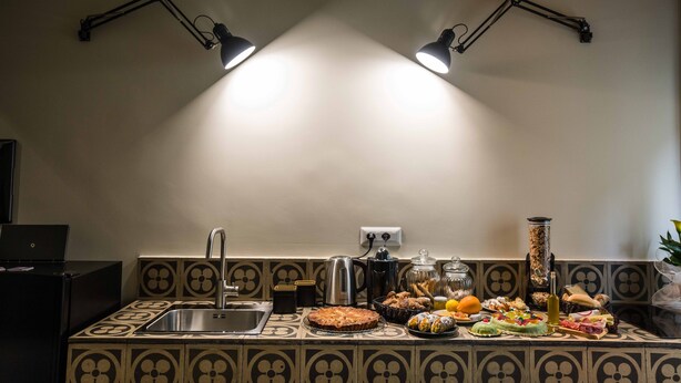Una cocina con salpicadero de azulejos, un lavabo, una cafetera y diversos alimentos en la encimera.