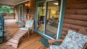 A wooden deck with outdoor seating, a covered area, and a view into a room with a fireplace. - Spacious Boone log cabin with 4 bedrooms, 3 baths, river access and game room (Boone)