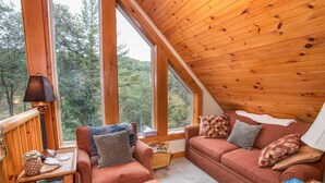 A cozy cabin interior with a wooden ceiling, large windows, a sofa set, and a lamp. - Spacious Boone log cabin with 4 bedrooms, 3 baths, river access and game room (Boone)