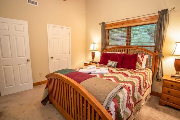 A bedroom with a wooden bed, a nightstand, a lamp, a window with curtains, and a door. - Spacious Boone log cabin with 4 bedrooms, 3 baths, river access and game room (Boone)
