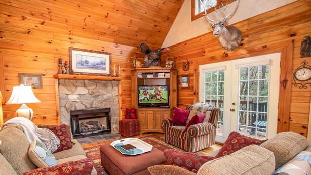 A cozy log cabin interior with a fireplace, comfortable seating, a television, and a deer head decoration. - Spacious Boone log cabin with 4 bedrooms, 3 baths, river access and game room (Boone)