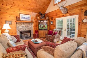 A cozy log cabin interior with a fireplace, comfortable seating, a television, and a deer head decoration. - Spacious Boone log cabin with 4 bedrooms, 3 baths, river access and game room (Boone)