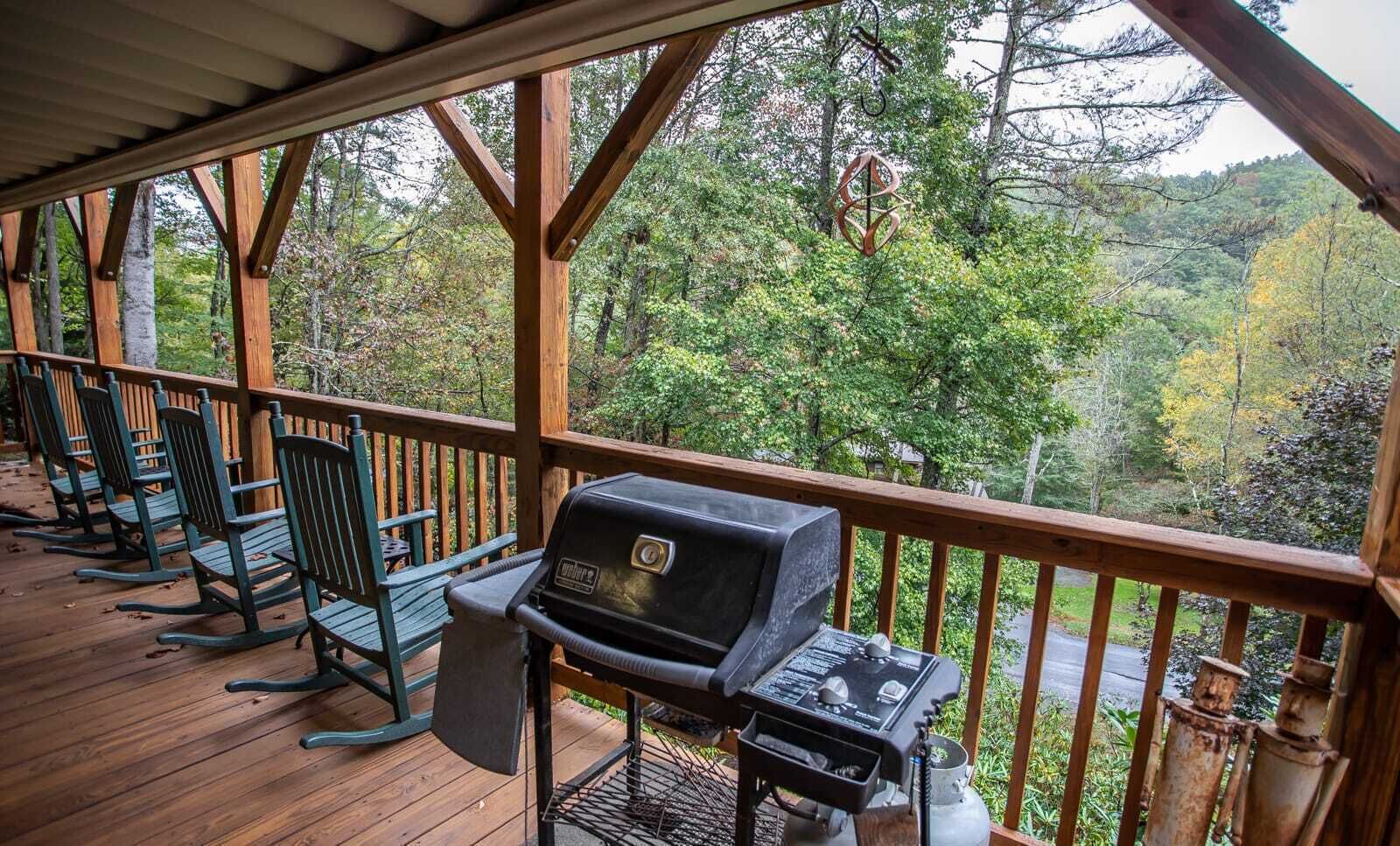 A covered outdoor deck with a grill and rocking chairs.