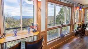 Un interior rústic amb grans finestres, bigues de fusta i una zona de bar amb tamborets i un cartell de neó.