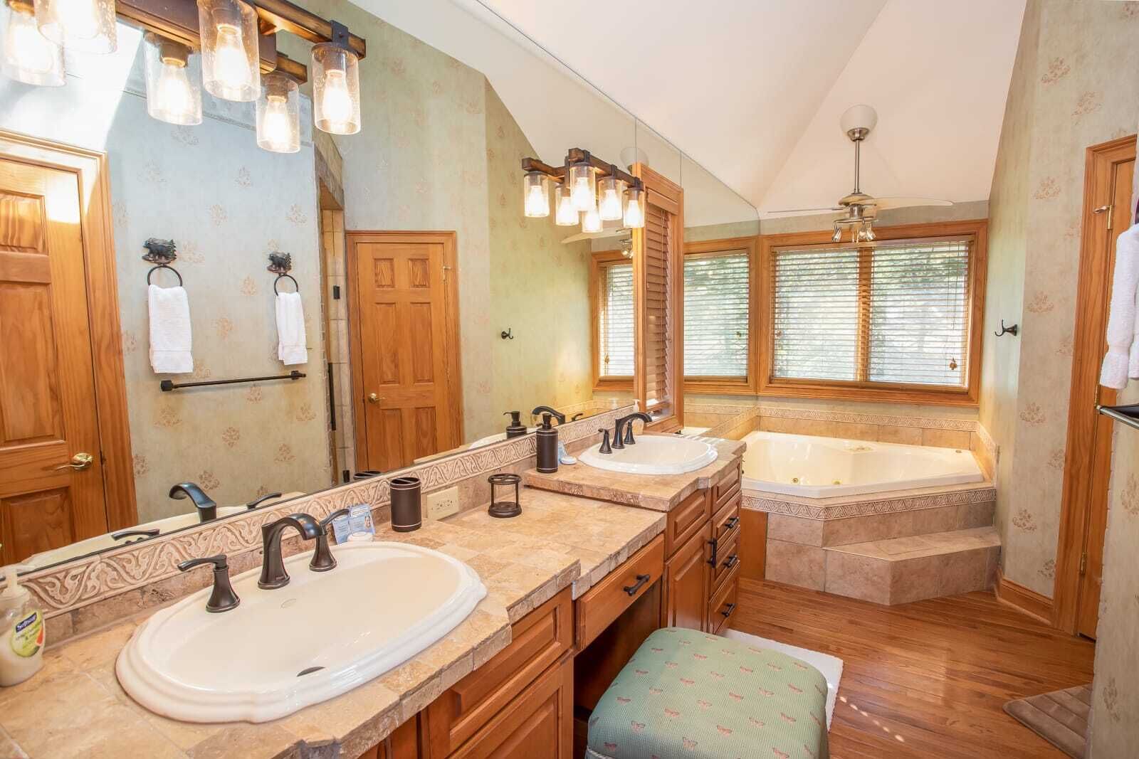 Une salle de bain avec deux lavabos, une grande baignoire et une fenêtre avec des stores.