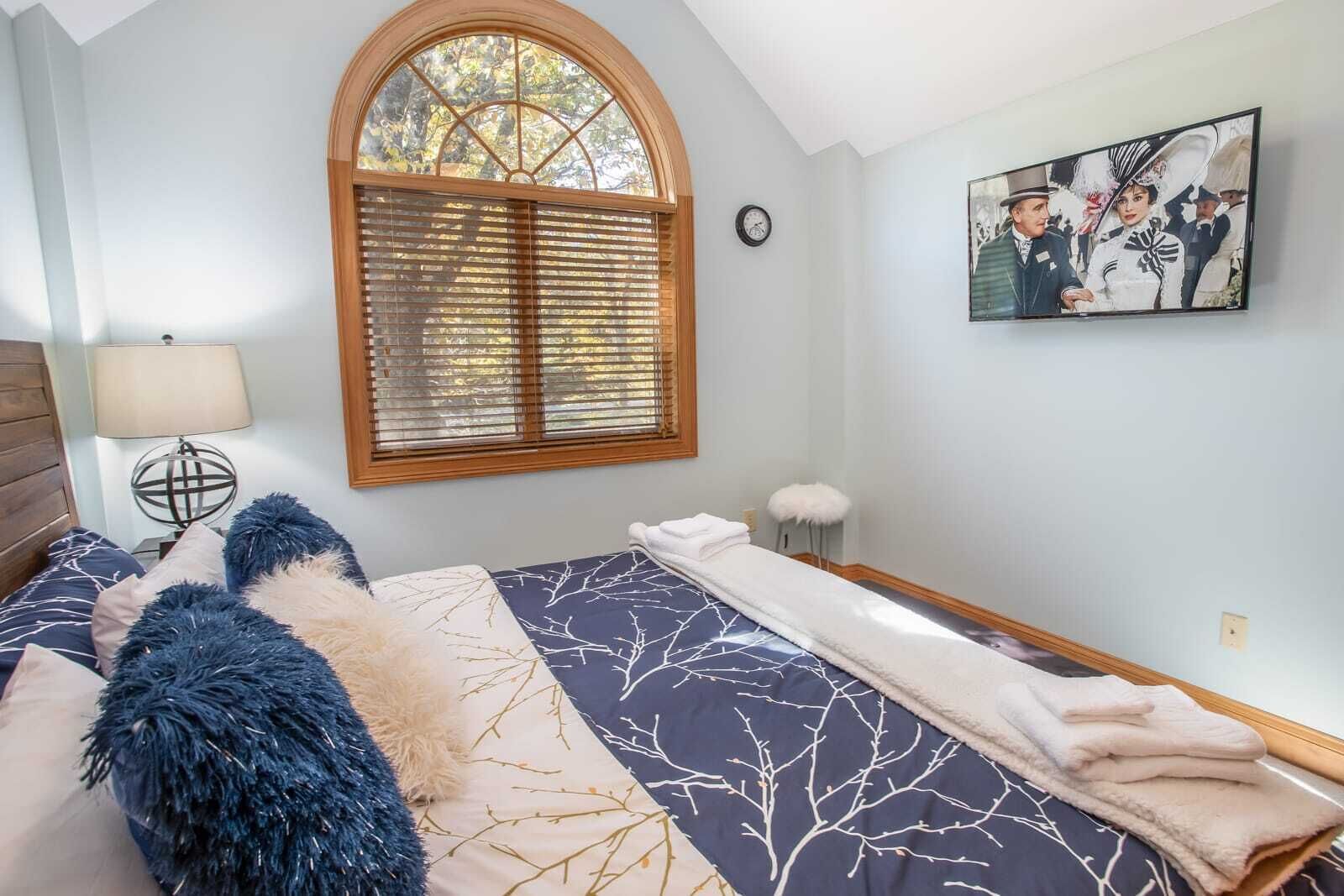 Une chambre à coucher avec un lit, une fenêtre avec des stores, une horloge, une lampe et un tableau au mur.