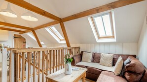 Une chambre à coucher aménagée dans un espace de type « loft », avec un plafond en bois, un canapé en cuir marron, une table en bois et une lucarne.