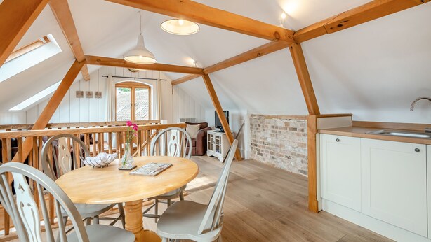 Un loft spacieux avec un coin repas en bois, une cuisine dotée d’un pare-feu en pierre et une vue dégagée sur l’extérieur grâce à une grande fenêtre.