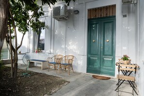 Un edificio con puerta verde, una banca y dos sillas de mimbre en el exterior.