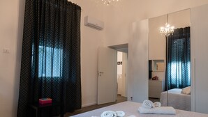 Une chambre d’hôtel avec un lit, une chaise, un bureau, un miroir et une fenêtre avec des rideaux.