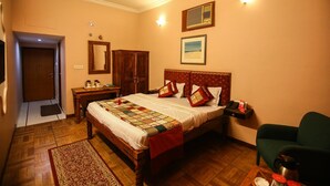 A bedroom with a wooden bed, a nightstand, a desk, a chair, a heater, and a door. - Pioneer Plaza Jodhpur (Jodhpur)