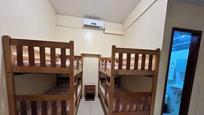 Una habitación con literas, una mesita de noche pequeña y un baño visible a través de una puerta abierta.