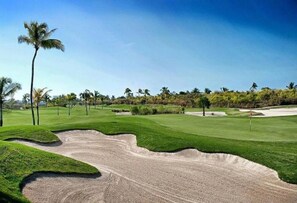 A golf course with sand bunkers, palm trees, and a clear blue sky.