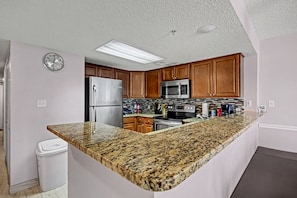 Cocina con encimeras de granito, electrodomésticos de acero inoxidable, gabinetes de madera y microondas integrado.