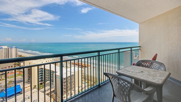 A balcony with a view of the beach and ocean, a table, and chairs. - Beauty on The Beach! (Myrtle Beach)
