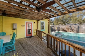 Une terrasse en bois avec une piscine, une porte rouge et un mur jaune.
