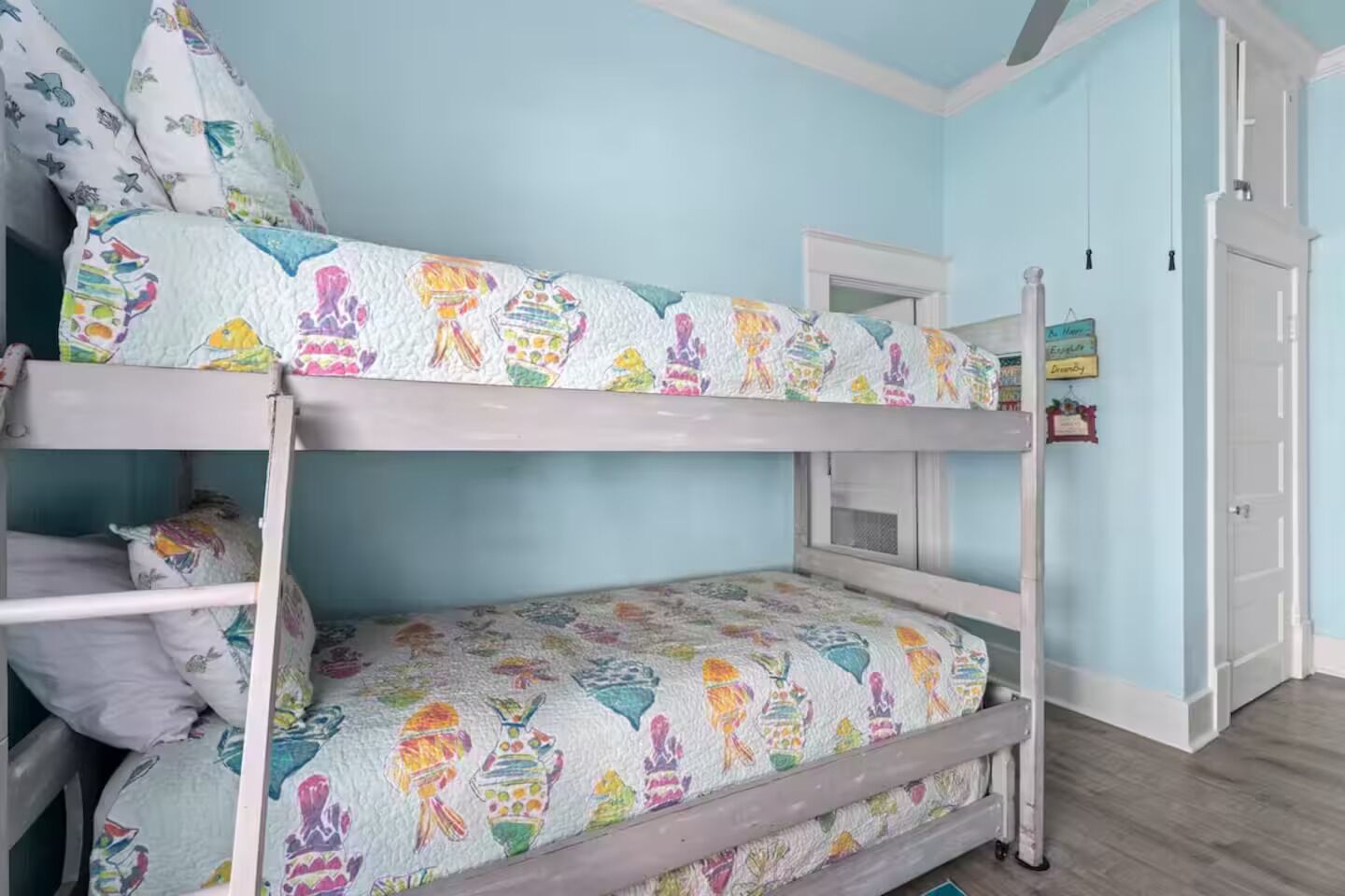 A bunk bed with colorful fish-patterned bedding, a white door, and a light blue wall.