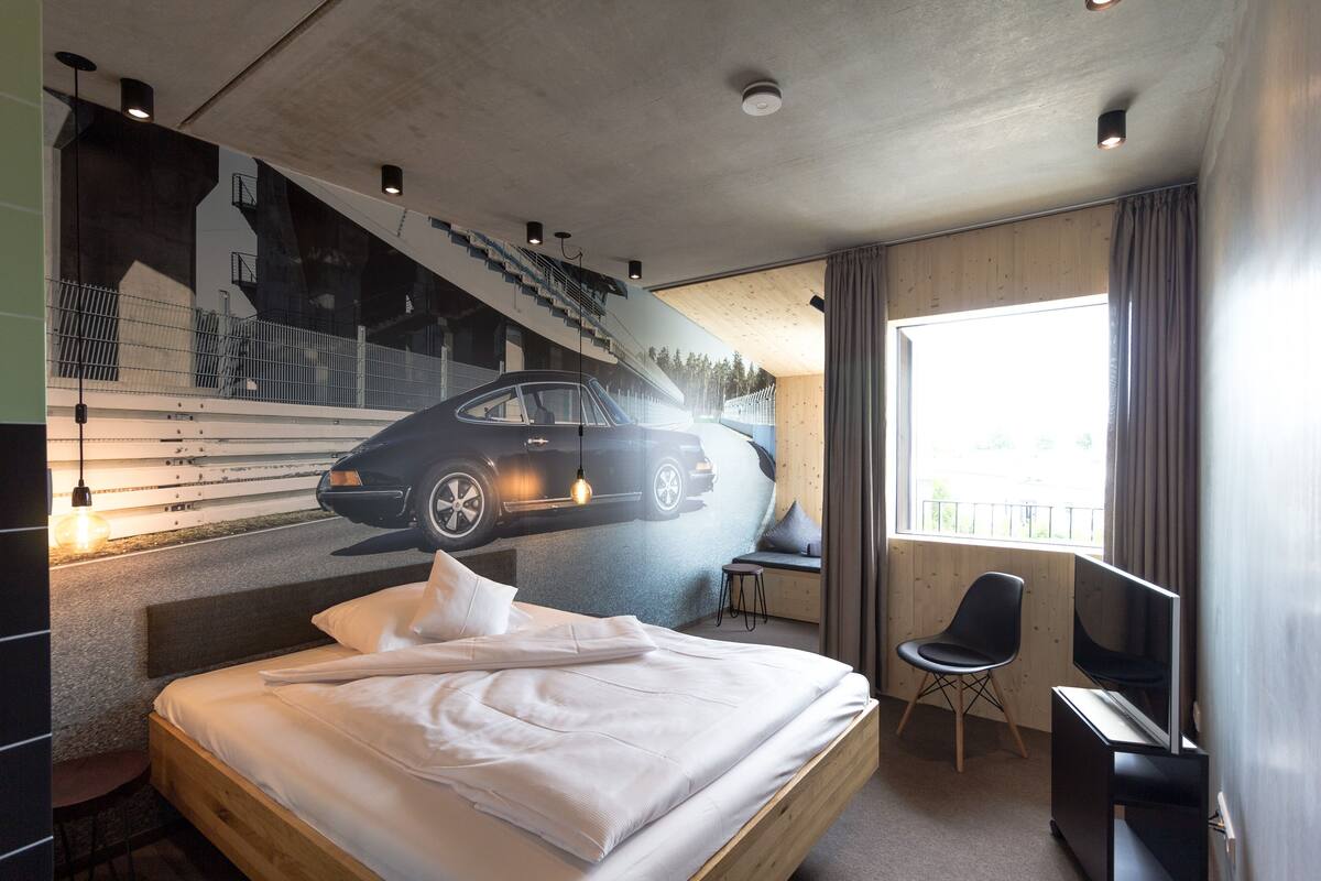 Una habitación de hotel moderna con cama, escritorio, silla, televisión y un ventanal grande.