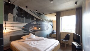 Una habitación de hotel moderna con una cama grande, un escritorio con silla, televisor y ventana con cortinas.
