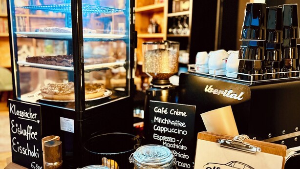Mostrador de café con una exhibición de pasteles, una máquina de café y un tablero de menú.