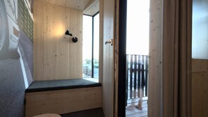 Una habitación con techo de madera, un banco, una pequeña mesa y una puerta que da a un área exterior con balcón.
