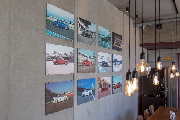 A wall with multiple framed photographs of cars and a modern kitchen area with hanging light fixtures.