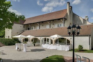 Une cour avec des tables disposées pour les repas, un bâtiment doté d’un toit en tuiles et un lampadaire.