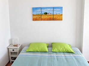 Ein Schlafzimmer mit einem Bett, zwei Kissen, einem Nachttisch und einem Wandbild.