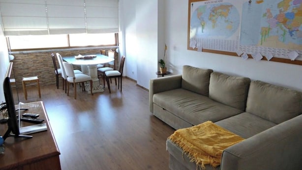 Ein Wohnzimmer mit einer Couch, einem Esstisch mit Stühlen, einem Fernseher und einer Pinnwand mit Weltkarten.