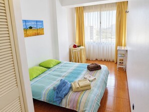 A bedroom with a bed, pillows, a bedside table, a chair, and a window with curtains.