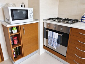 Eine Küche mit Mikrowelle, Gasherd, Holzschränken und einem Edelstahlbackofen.