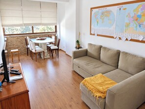 Ein Wohnzimmer mit einem runden Esstisch, Stühlen, einer Couch, einem Fernseher und einer Pinwand mit Karten.