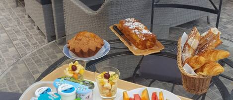 An outdoor dining area with wicker furniture, a glass table, and a variety of food and drinks.