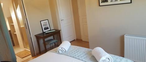 A hotel room with a bed, a desk with a computer, a framed picture on the wall, and a radiator.