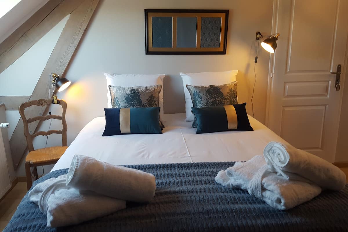 Quarto com uma cama, duas luminárias de cabeceira, uma cadeira e uma janela.