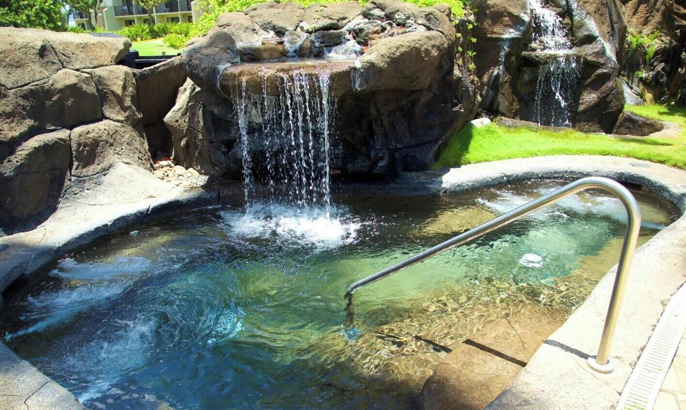 A clear pool with a metal ladder and a waterfall feature.