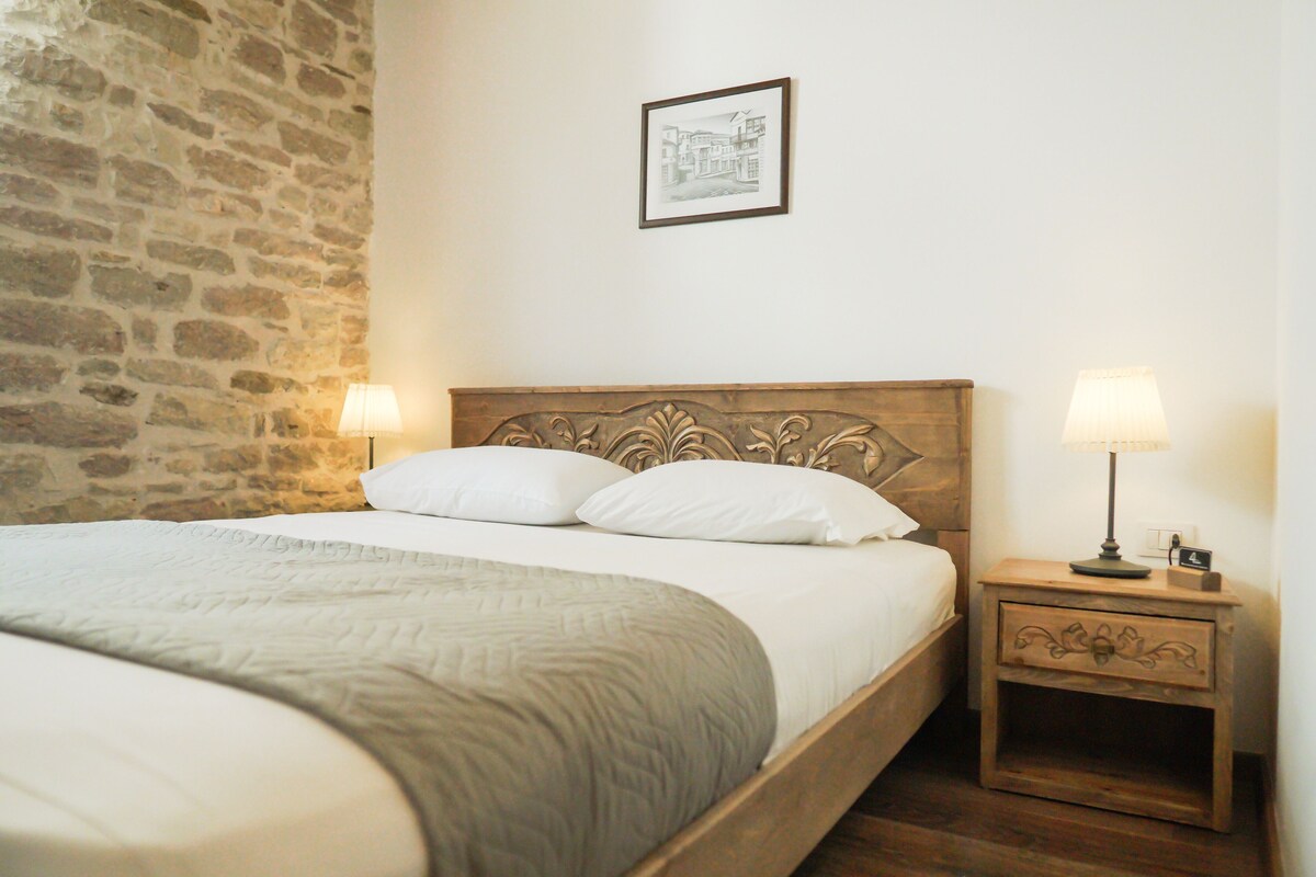 A neatly made bed with a wooden headboard, two bedside lamps, and a small nightstand with a lamp.