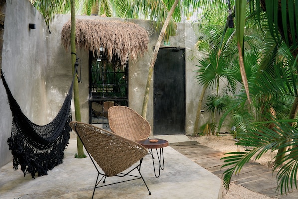 Una hamaca, sillas de mimbre y una estructura de techo de paja en un jardín tropical.
