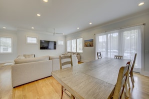 A spacious living area with a large wooden dining table, a sofa, and a television mounted on the wall.