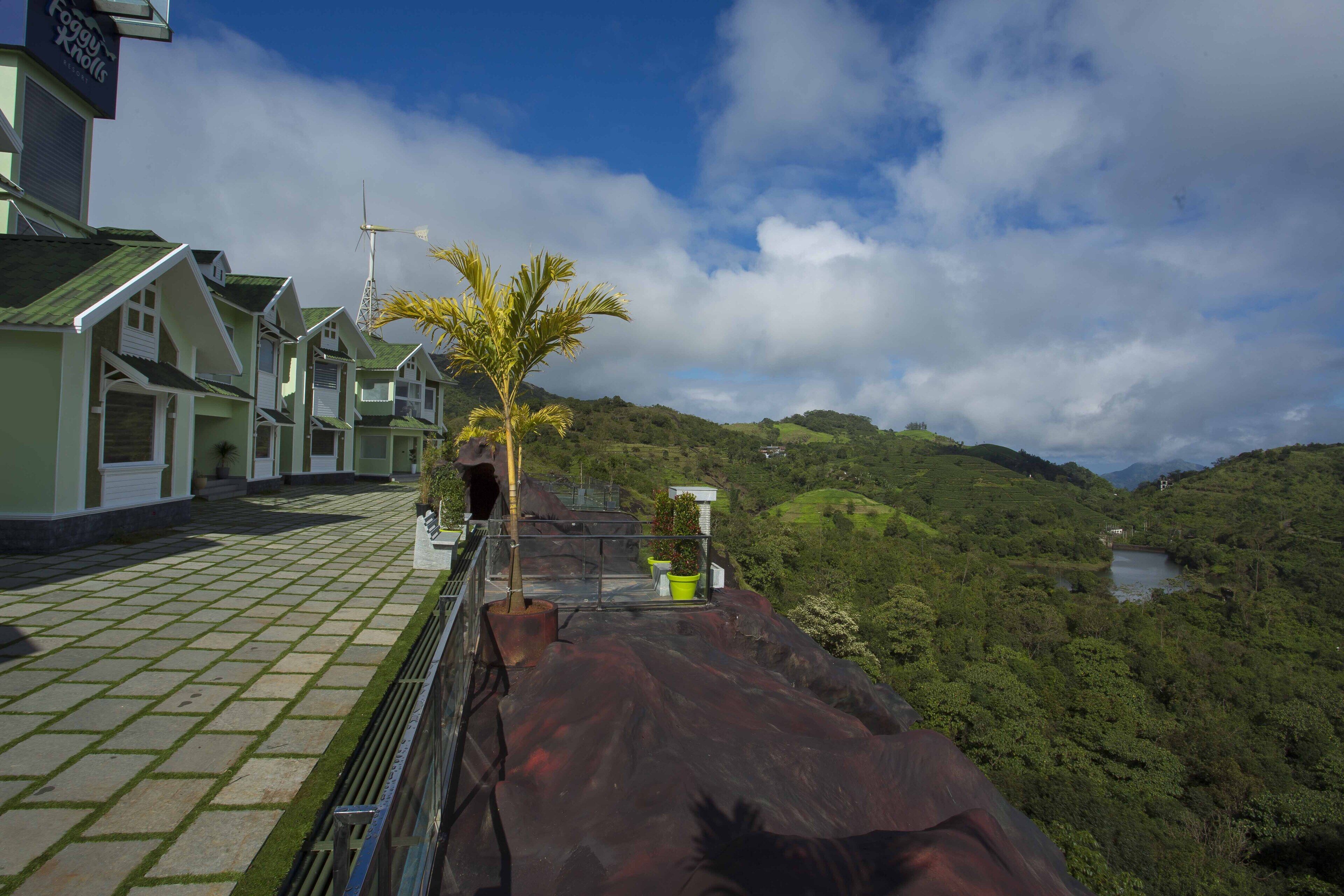A hotel with a paved walkway, a palm tree, and a view of a lake surrounded by hills.