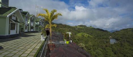 A hotel with a paved walkway, a palm tree, and a view of a lake surrounded by hills.