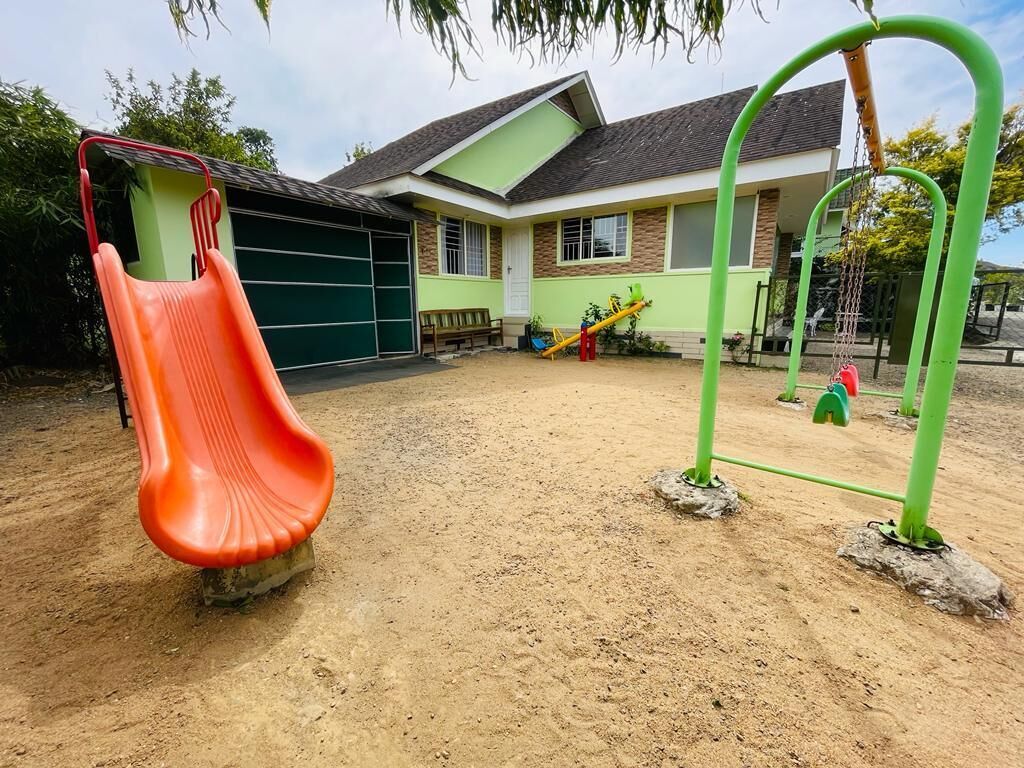 Un patio de juegos con tobogán y columpios frente a una casa.