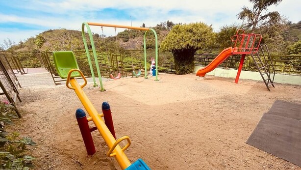 Un parque infantil con zona de juegos de arena, un tobogán verde y uno rojo.