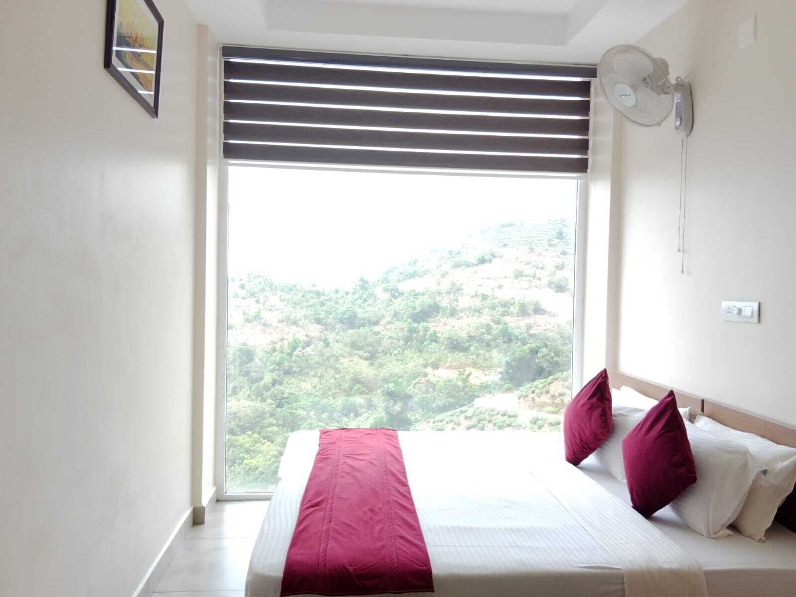 Una camera da letto con un'ampia finestra, un letto con coperta rossa e un ventilatore a parete.