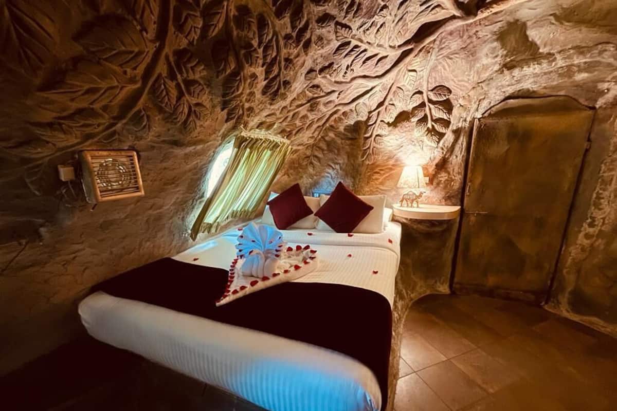 A bedroom with a bed, pillows, a bedside table, and a wall with carved rock patterns.