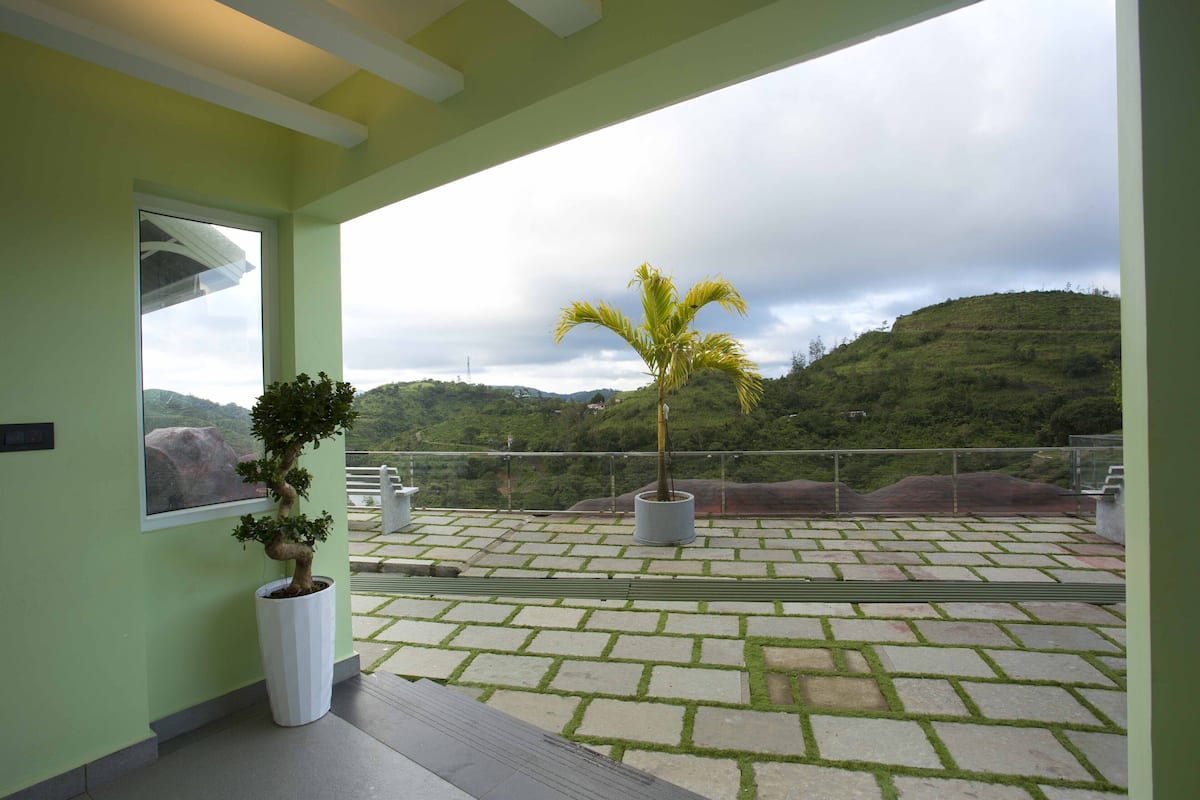 A rooftop terrace with potted plants, a view of green hills, and a stone-patterned floor.